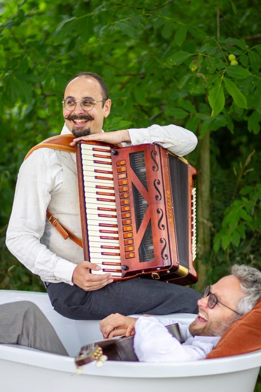 Alain Decroix à l’accordéon et Romain Verwilghen à la guitare, souriants, dans une baignoire en extérieur
